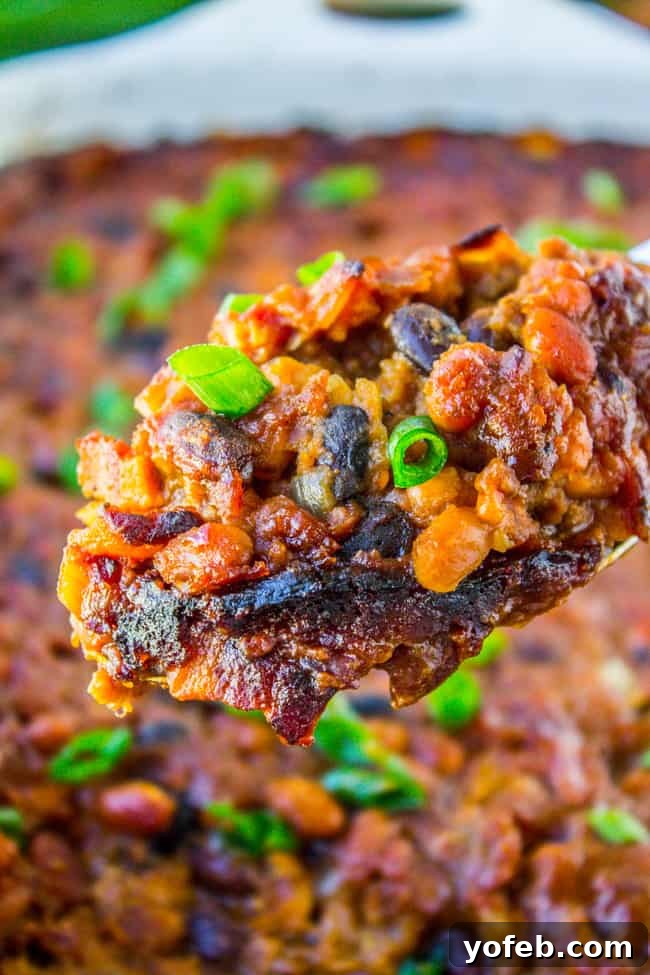 Crispy Bacon Bean Bake 2 A serving spoon lifting a spoonful of rich, saucy bacon beef baked beans from a pan.