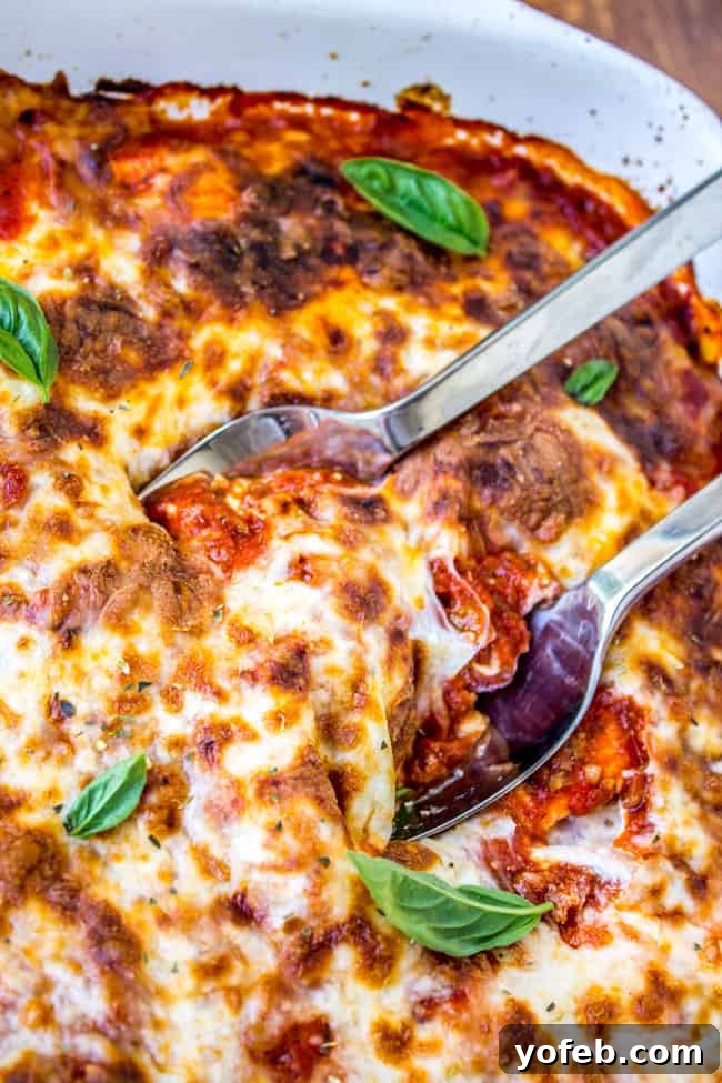 Lazy Lasagna with Ravioli 3 Two metal spoons scooping into a large pan of bubbling ravioli lasagna.