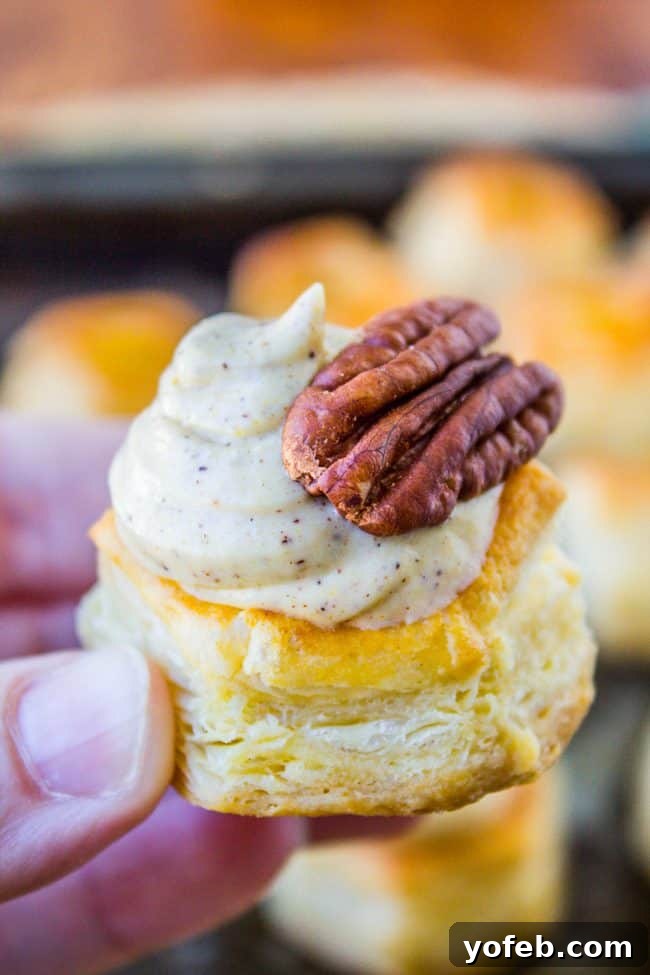 Pillowy Pumpkin Cream Cheese Puffs 5 A hand holds a flaky pastry topped with creamy pumpkin spiced filling and a whole pecan, with more pastries blurred in the background.