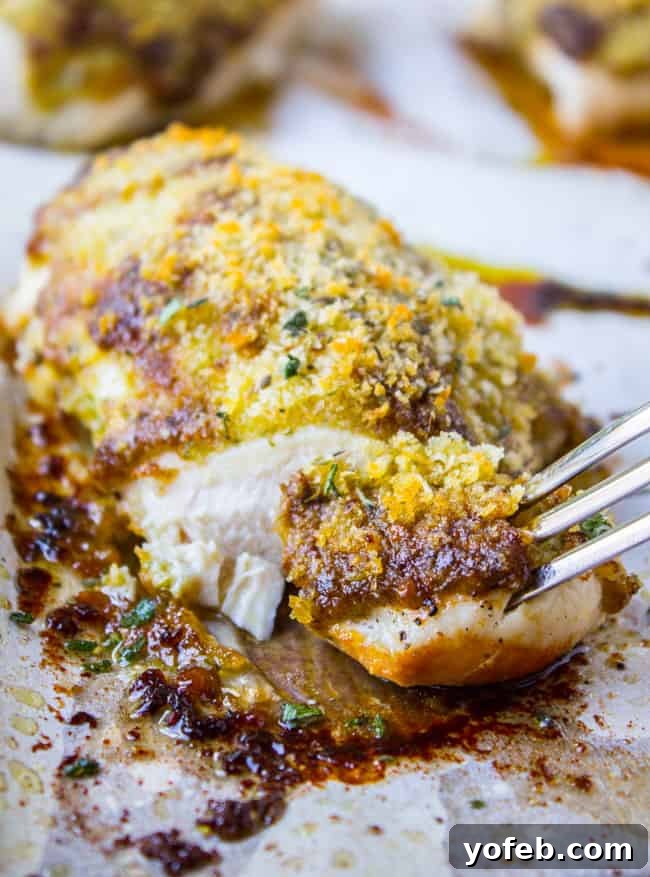 Easy Baked Pesto Chicken from The Food Charlatan. This quick Easy Baked Pesto Chicken recipe comes together in about 30 minutes! Can't beat that. I love it because I almost always have these ingredients on hand so it's a good last minute dinner. #pesto #chicken #baked #basil #oven #healthy #chickenbreast #easy A fork taking a bite of golden-brown baked pesto chicken, showcasing its crispy exterior and tender interior.