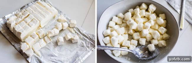A knife cutting cold cream cheese into small, even cubes on a cutting board, preparing it for inclusion in the scone dough.
