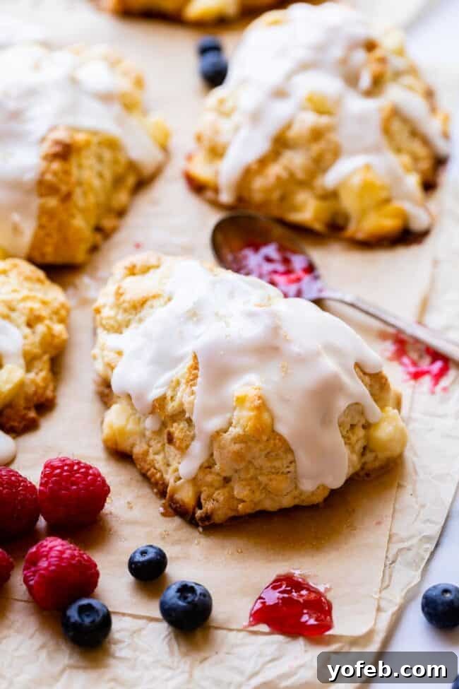 Freshly baked glazed scones on a baking sheet, surrounded by vibrant fresh fruit and a spoon laden with jelly, ready for a delightful breakfast spread.