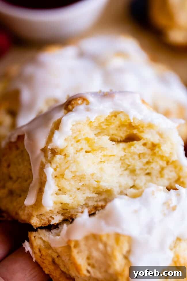 The flaky, layered interior of a glazed scone is revealed after being broken in half, showcasing its tender texture.