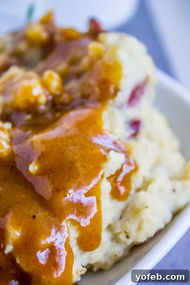 Perfectly smooth and flavorful make ahead turkey gravy, ready for your Thanksgiving feast. Homemade turkey gravy dripping luxuriously over a mound of creamy red mashed potatoes.