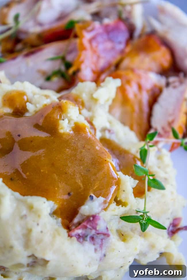 Make Ahead Turkey Gravy: The perfect accompaniment to roast turkey and mashed potatoes. Golden-brown turkey gravy generously coats red mashed potatoes, garnished with fresh thyme, beside slices of roasted turkey.