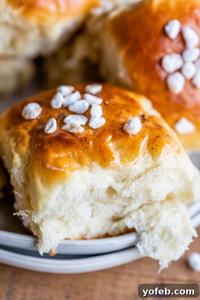 A single Swedish cardamom roll, beautifully golden brown and topped with pearl sugar, rests on a ceramic plate. The plate sits on a rustic wooden surface, highlighting the roll's inviting texture and sugar crystals.