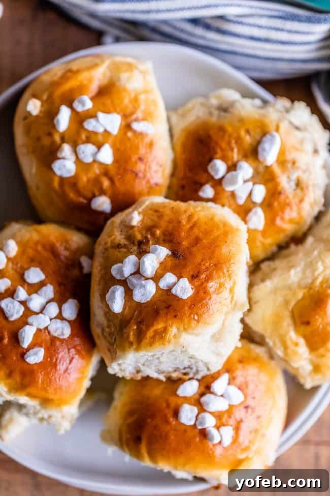 A stack of freshly baked cardamom buns, generously topped with glistening pearl sugar, rests on a plate. A blue dishtowel lies in the background, adding a touch of rustic charm to the scene.