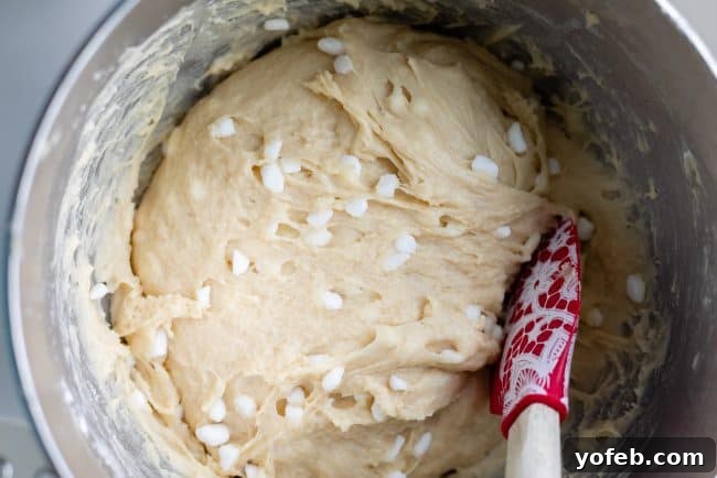 A close-up of light-colored dough, speckled with white pearl sugar granules, being mixed. The dough has a soft, pliable texture, indicating it's ready for its next step in the baking process.