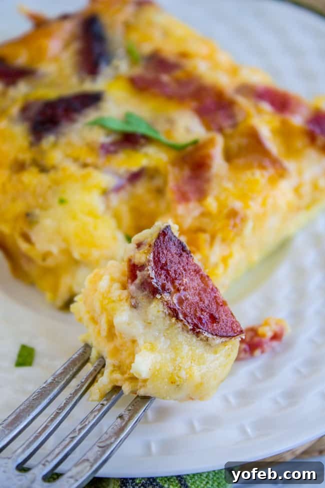 Savoring a Bite of Overnight Bacon and Egg Casserole A fork lifting a bite of cheesy egg casserole from a white plate