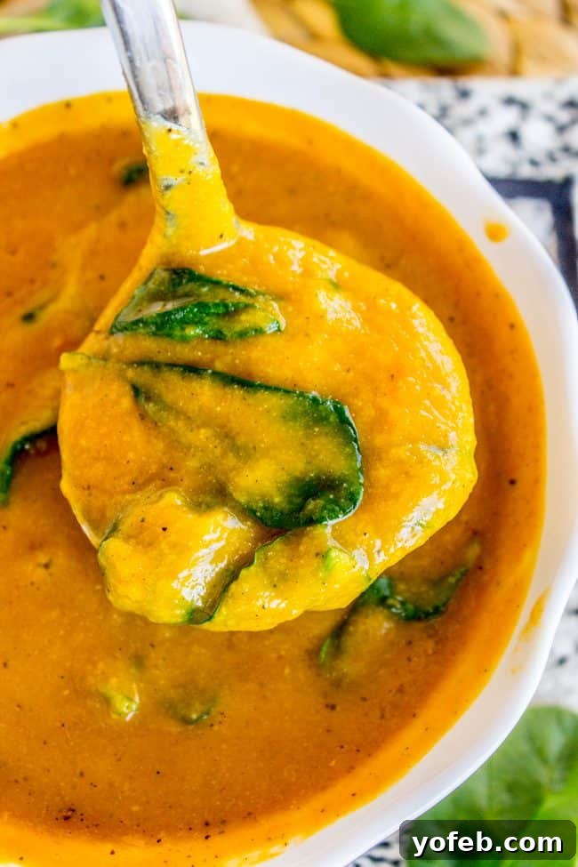 Creamy Vegan Cauliflower Soup 5 a spoonful of golden cauliflower soup with spinach in a white bowl.