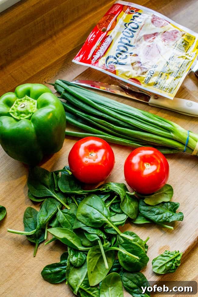 Pizza Egg Muffins: Effortless Weekday Breakfast 4 Fresh ingredients for Pizza Egg Muffins, including pepperoni, tomatoes, green onion, spinach, and green bell pepper on a rustic wooden countertop.