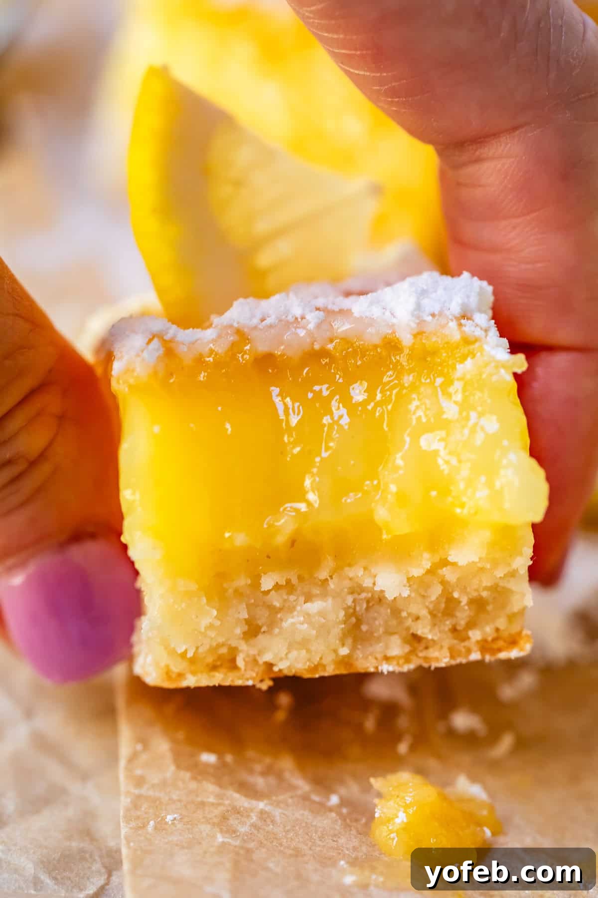 Seriously Zesty Lemon Bars My Absolute Best 22 thumb and finger holding a lemon square with a bite taken from it.