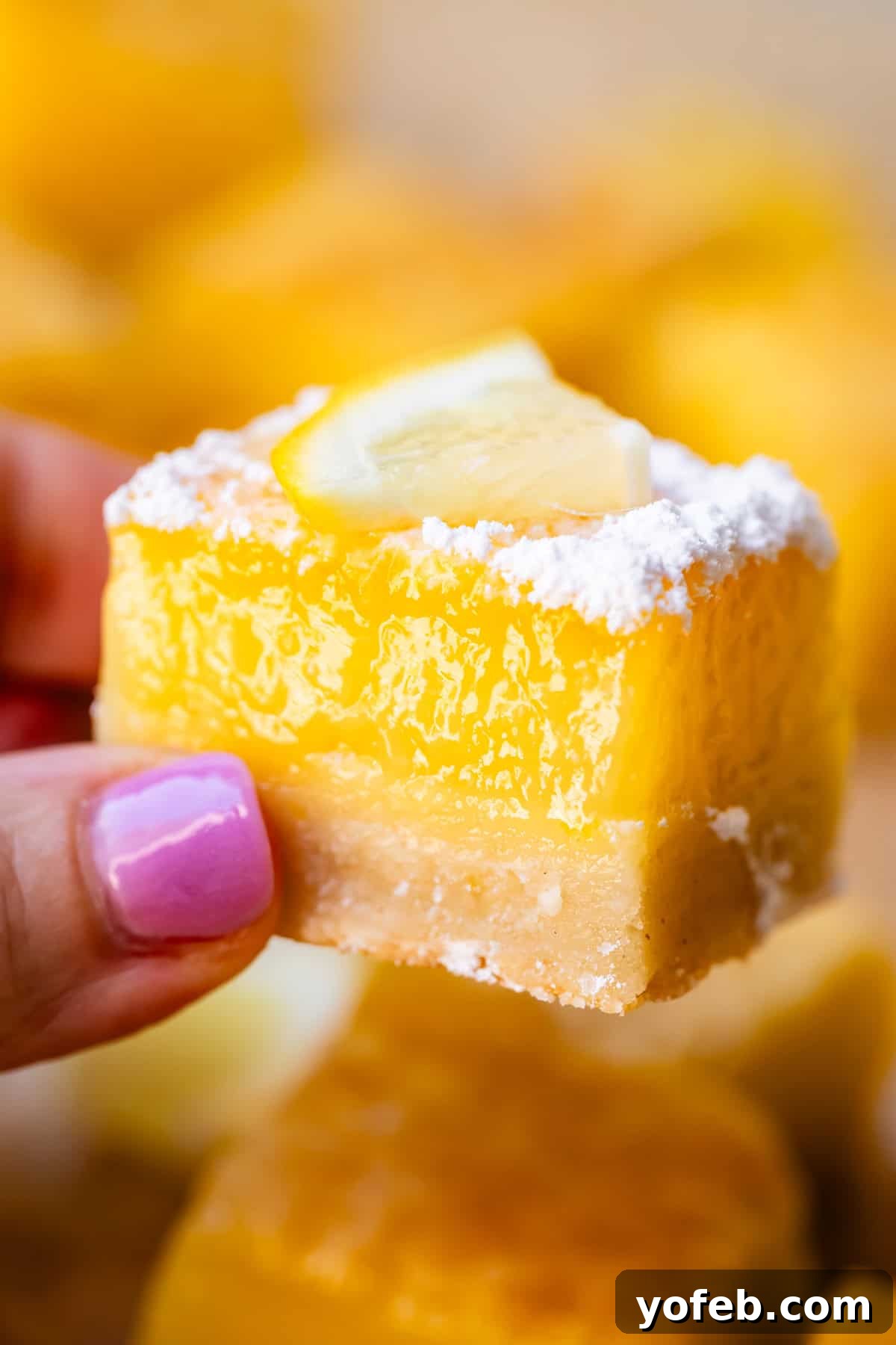 Seriously Zesty Lemon Bars My Absolute Best 4 finger and thumb holding up a chunky lemon square to show the hefty filling.
