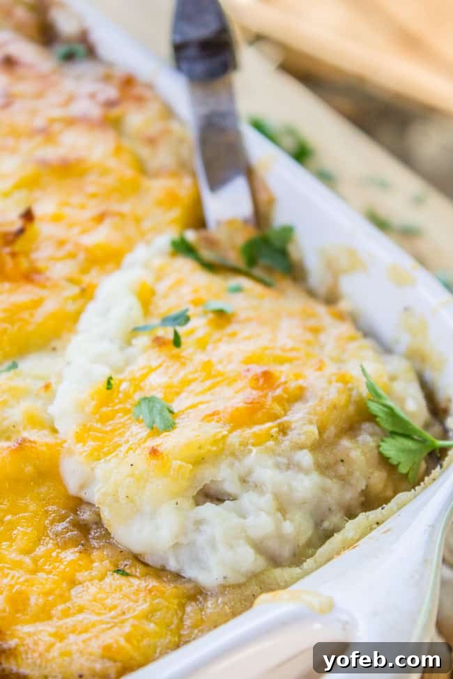 Ultimate Cheesy Shepherds Pie 5 a large metal spoon serving a portion of cheese-topped shepherd's pie from a baking dish.