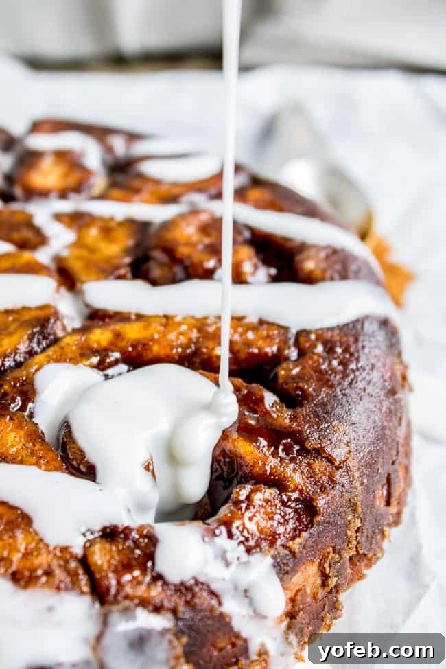 Quick No Yeast Cinnamon Rolls 4 Creamy icing being generously drizzled over a pan of warm, flaky cinnamon rolls.