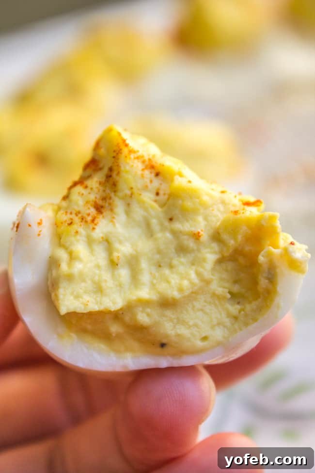 Timeless Deviled Eggs 3 A half-eaten deviled egg showing its creamy, rich filling, garnished with paprika.