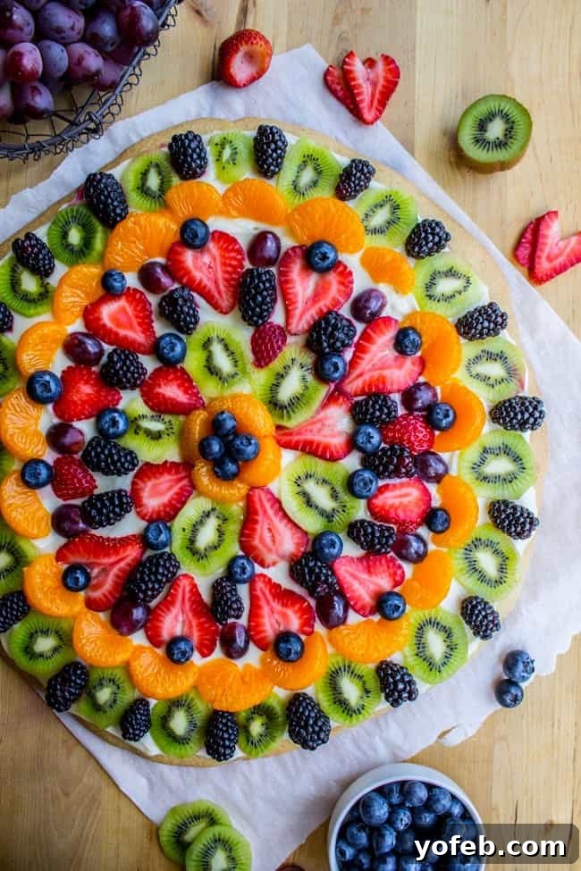 Pillowy Sugar Cookie Fruit Pizza Delight 26 An older overhead photo of a sugar cookie based fruit pizza, topped with strawberries, mandarin oranges, blueberries, kiwi, and blackberries, with cream cheese frosting.