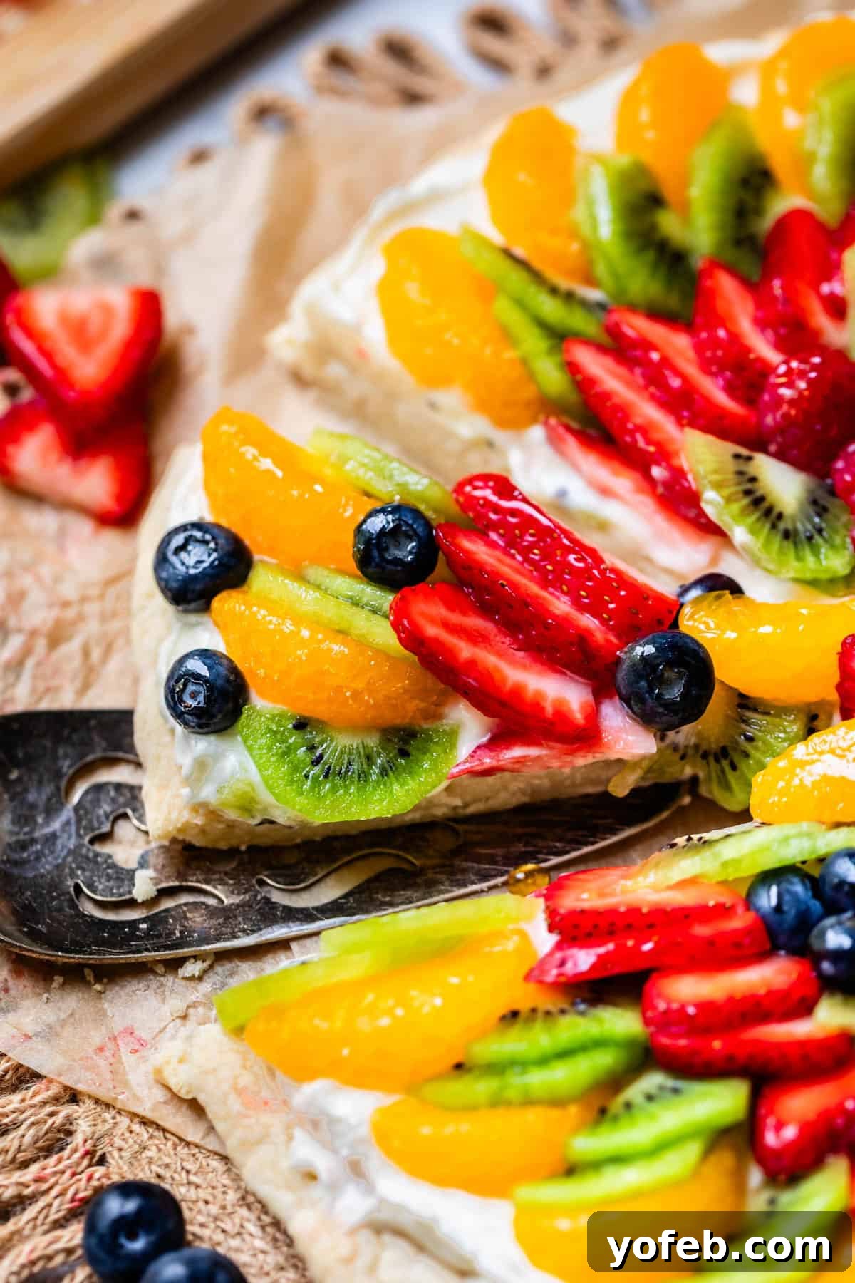 Pillowy Sugar Cookie Fruit Pizza Delight 4 A serving spatula carefully lifting a perfect slice of fruit pizza from the whole, beautifully decorated dessert.