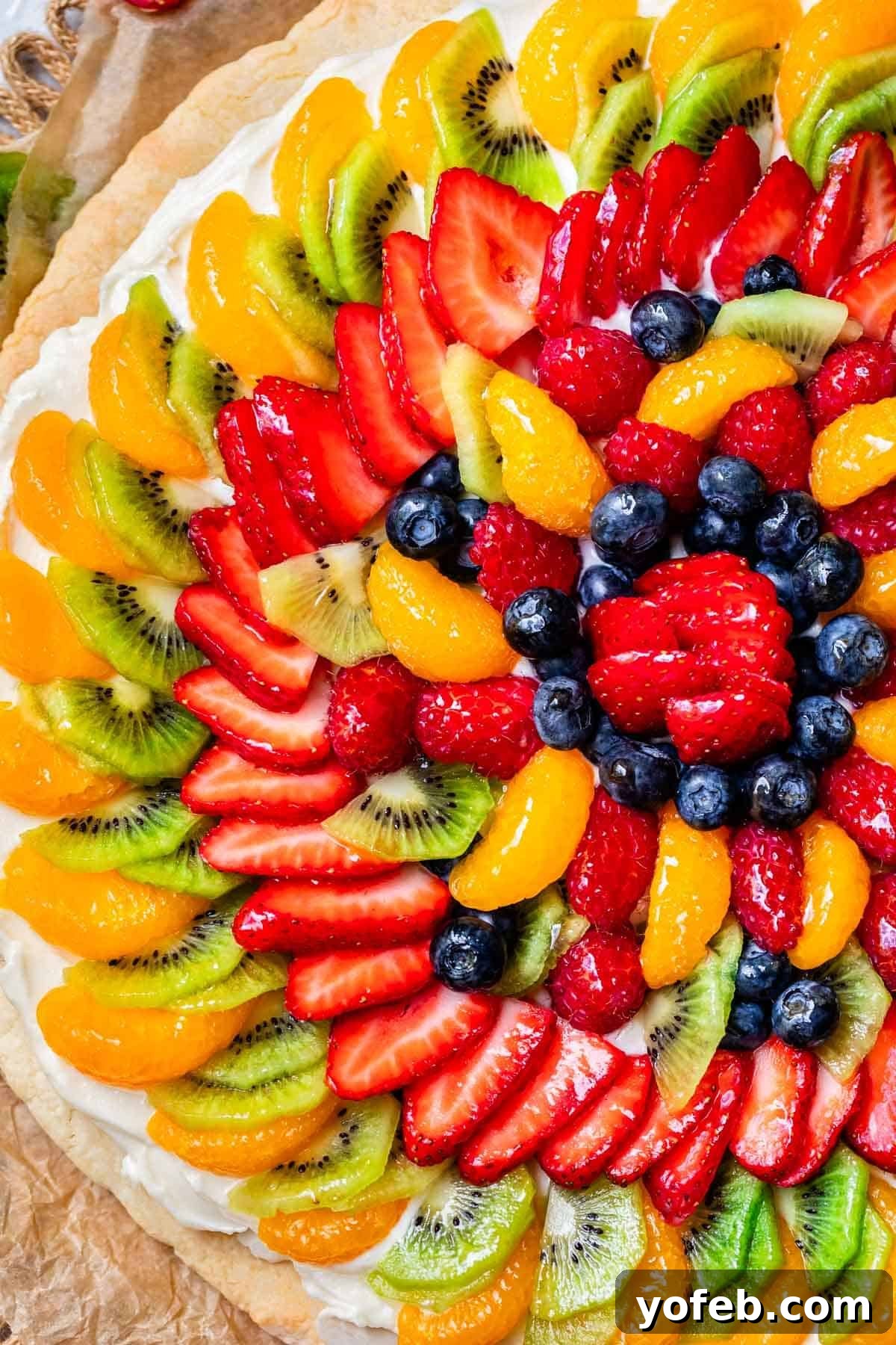 Pillowy Sugar Cookie Fruit Pizza Delight 5 An overhead view of a circular fruit pizza, showcasing layers of colorful fresh fruit meticulously arranged on the creamy frosting and tender cookie crust.