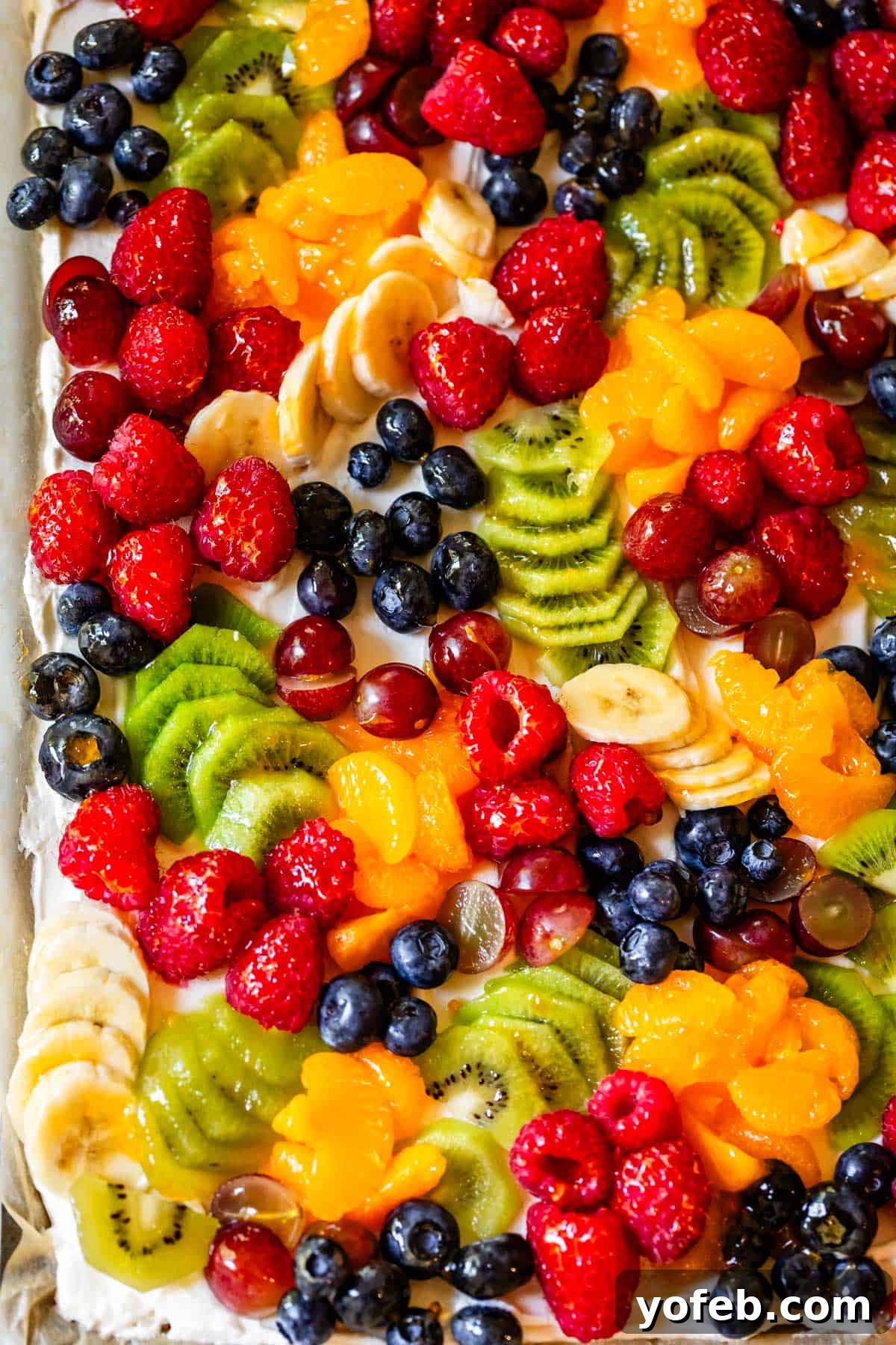 Pillowy Sugar Cookie Fruit Pizza Delight 7 An overhead shot of a rectangular fruit pizza, artfully arranged with various fruits in distinct groupings, resembling a dessert charcuterie board.