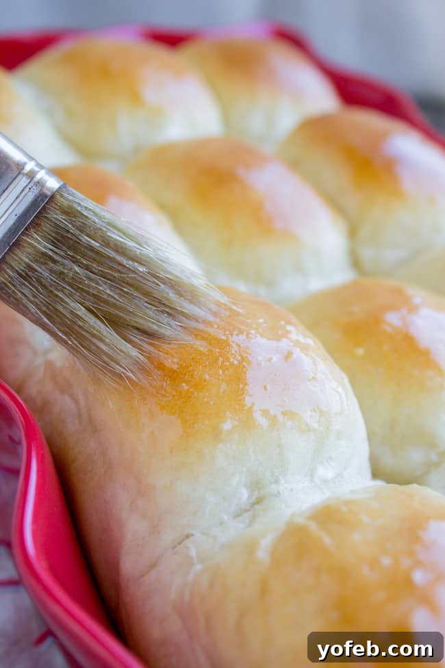 Aunt Shirley's Signature Dinner Rolls 4 A hand brushing melted butter over hot, golden brown homemade dinner rolls, enhancing their shine and flavor.