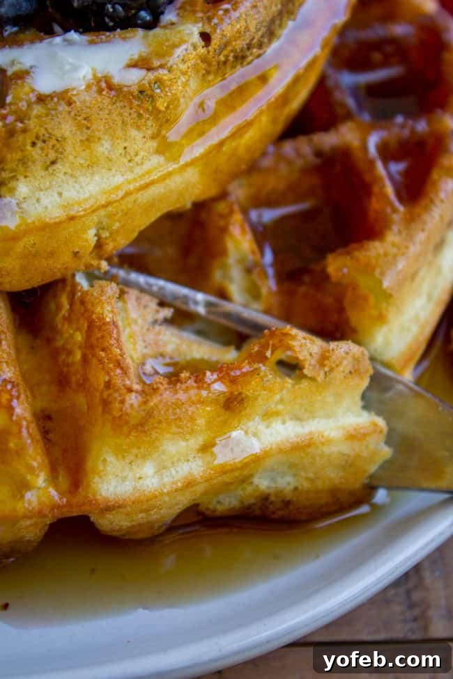 Enjoying Fluffy Waffles with Syrup A fork gracefully cuts into a stack of warm, syrup-covered homemade waffles, revealing their fluffy interior.