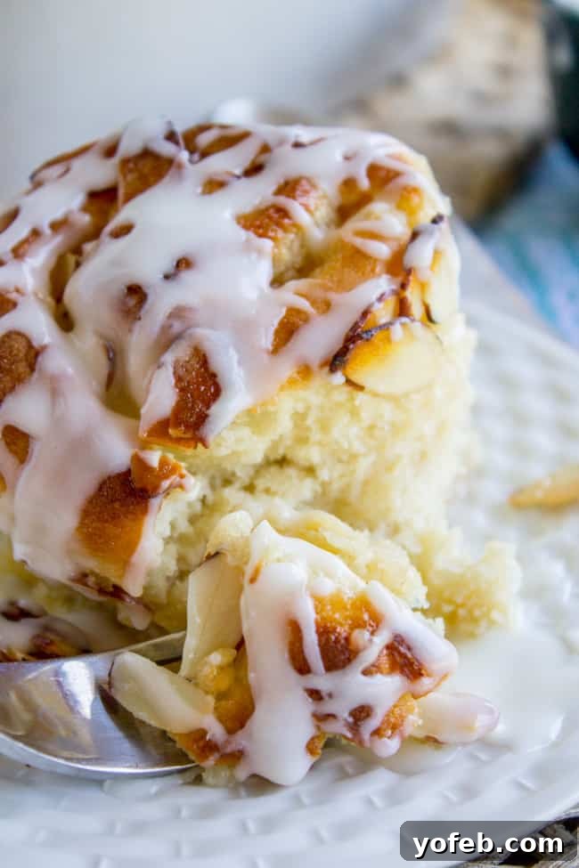 Golden Hour Almond Swirls 5 Close-up of a single honey almond roll, showcasing the crunchy topping and a sweet glaze drizzle.