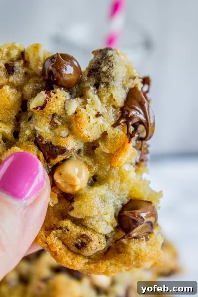 Texas Cowboy Cookies from The Food Charlatan. Everything's bigger in Texas and these Cowboy cookies (sometimes called Texas Cow Chips) are no exception. They are crispy on the edges but chewy and moist in the middle, and have about a hundred mix-ins that all combine to create the Texas of all cookies. #texas #cowboy #cookies #chocolatechip #chocolate #peanutbutterchips #oatmeal #coconut #pecans #crispy #crunchy A mouth-watering close-up of a single Texas cowboy cookie, showcasing its rich texture and diverse mix-ins.