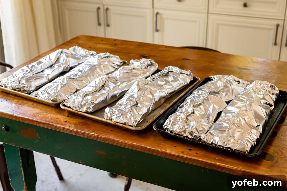 Nana's Irresistible Fall-Off-The-Bone Ribs with Barb's Signature Barbecue Sauce 7 Six racks of pork ribs meticulously wrapped in heavy foil on baking sheets, awaiting their slow roast in the oven.