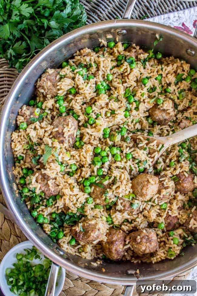 One Pan Meatball Rice Feast 5 A large metal skillet filled with a delicious mix of rice, meatballs, and peas being gently stirred.