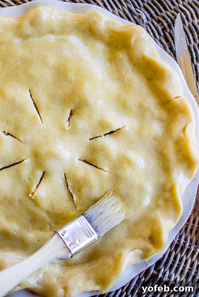 Classic Double Crust Chicken Pot Pie from The Food Charlatan. The BEST recipe for Chicken Pot Pie! Carrots, peas, and rotisserie chicken (or use leftover turkey from Thanksgiving!) come together in a deliciously flavorful gravy. All wrapped up in a buttery, flaky chicken pot pie crust! If you've only tried frozen pot pies from the store...please, I'm begging you, make this. #potpie #piecrust #chicken #homemade #fromscratch #flaky #butter #recipe A pastry brush applying an egg wash to the top of an unbaked chicken pot pie.