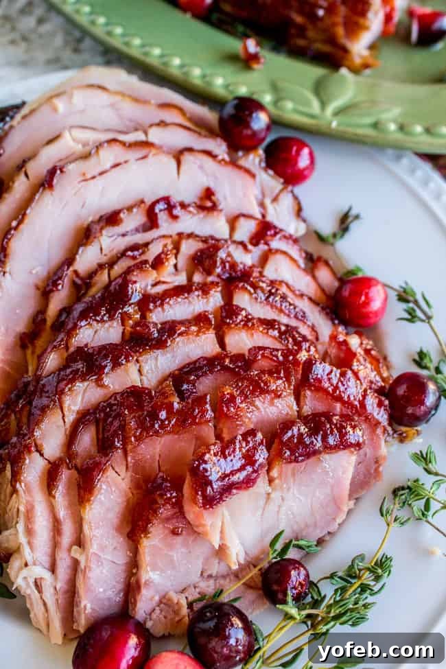 Succulent Roasted Ham with Sweet and Tangy Cranberry Dijon Glaze 2 Sliced glazed ham on a white plate with Cranberries and thyme