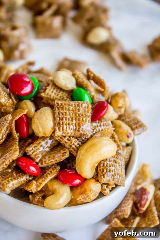 Sticky Sweet-and-Salty Chex Mix (Christmas Crack Recipe) from The Food Charlatan. I've got your yummy Christmas Crack recipe right here! This Sticky Sweet and Salty Chex Mix gets its name for good reason! Once you start you just can't stop. A simple syrup (with LOTS of butter) gets drizzled over corn Chex and studded with nuts and M&Ms. It is salty-sweet perfection! #christmascrack #christmas #chexmix #chex #m&m #sweetandsalty #dessert #yummy #syrup #candy Close-up of the sweet and salty chex mix recipe, showcasing a delectable blend of glazed Chex cereal, colorful M&M's, and crunchy nuts.