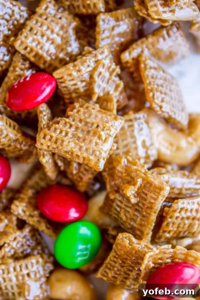 Sticky Sweet-and-Salty Chex Mix (Christmas Crack Recipe) from The Food Charlatan. I've got your yummy Christmas Crack recipe right here! This Sticky Sweet and Salty Chex Mix gets its name for good reason! Once you start you just can't stop. A simple syrup (with LOTS of butter) gets drizzled over corn Chex and studded with nuts and M&Ms. It is salty-sweet perfection! #christmascrack #christmas #chexmix #chex #m&m #sweetandsalty #dessert #yummy #syrup #candy A festive close-up of sweet and salty Chex mix, featuring a generous scattering of red and green M&M's.
