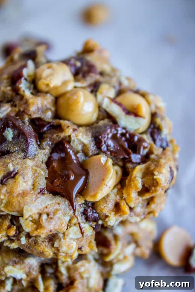 Skinny Texas Cowboy Cookies by The Food Charlatan. These low calorie cookies have NO sugar, NO white flour, and only 2 tablespoons of butter in the whole batch! What they do have are a ton of mix-ins. Oatmeal, coconut, bran flakes, pecans to name a few. They taste like a Texas Cowboy Cookie, but way better for you! (Which means I can eat half a batch...right?) #skinny #texascowboycookies #healthy #cookies #lowcalorie #nosugar #noflour #lowcarb #easy #recipes A stack of freshly baked Skinny Texas Cowboy Cookies with visible chocolate and peanut butter chips.