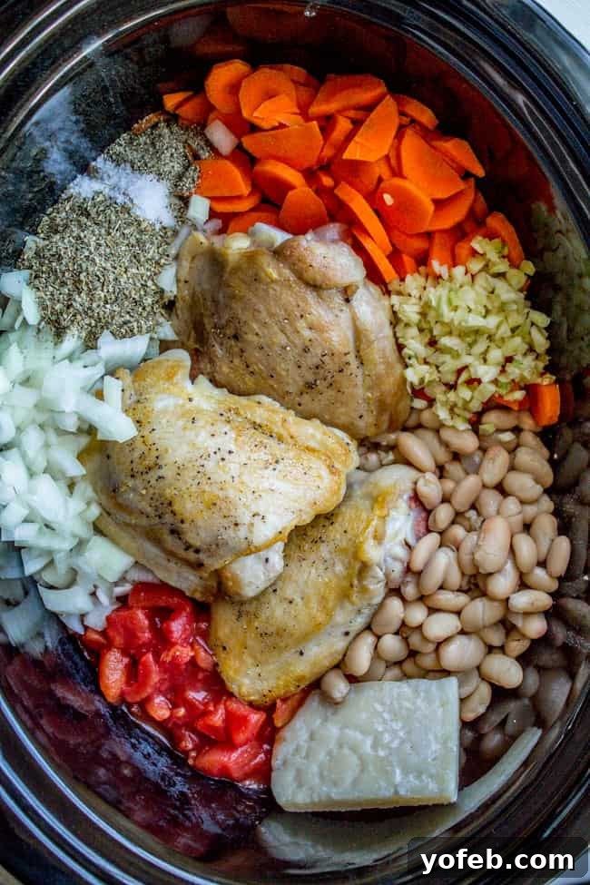 Effortless Slow Cooker Chicken, White Bean and Kale Soup 2 All the prepped ingredients including chicken, white beans, Parmesan rind, spices, and fresh vegetables in a slow cooker, ready for cooking.