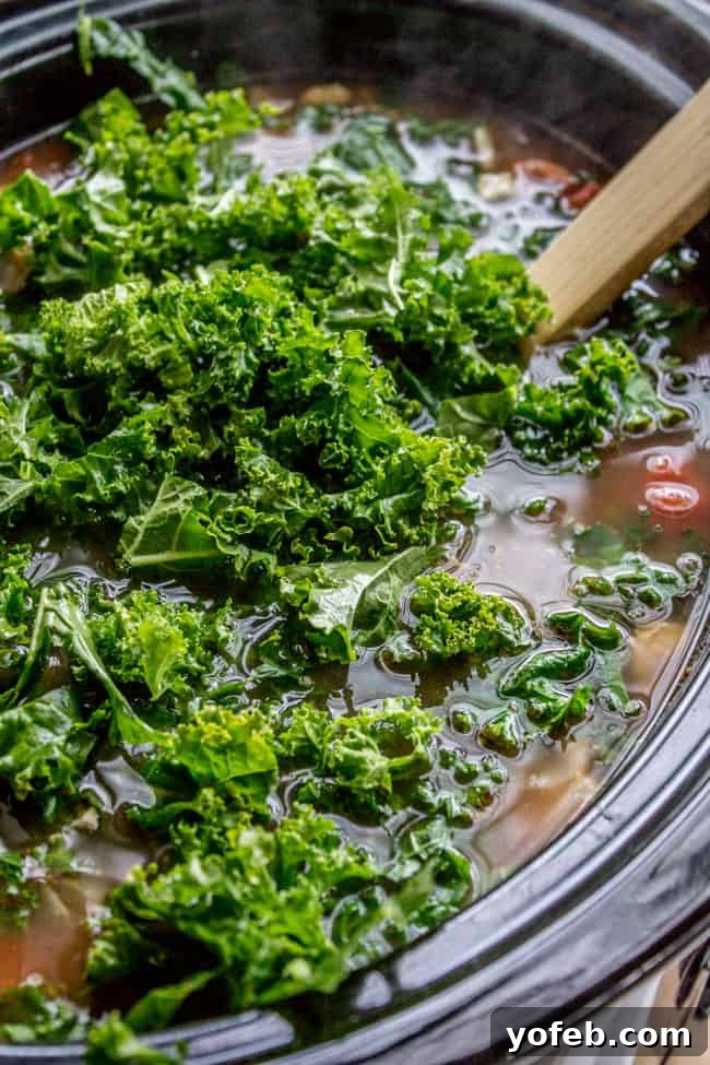 Adding Fresh Kale to Slow Cooker Soup Freshly chopped kale being added to a simmering slow cooker of chicken and white bean soup.