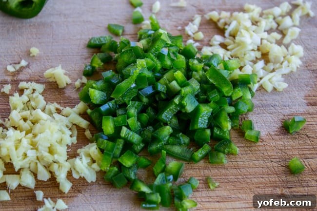Finely chopped garlic and deseeded jalapeno pepper on a wooden cutting board, prepped for sautéing.