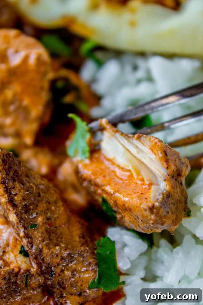 A fork lifts a tender piece of chicken tikka masala from a bed of jasmine rice, showcasing the creamy sauce and fresh cilantro garnish.