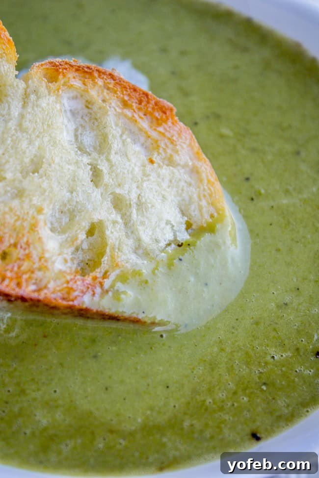 Vibrant 30-Minute Pea Soup 3 A slice of crusty baguette being dipped into a steaming bowl of homemade pea soup, highlighting its rich, creamy texture.