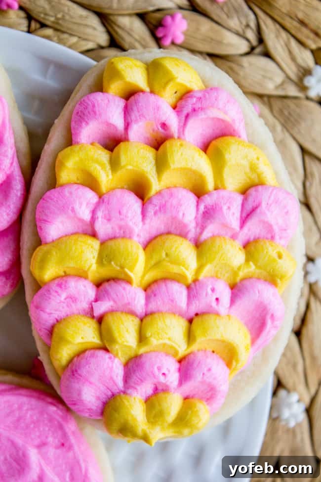The Softest Sugar Cookies of Your Life from The Food Charlatan. A secret ingredient in this sugar cookies recipe makes these cookies the SOFTEST and most flavorful cookies of your life! And they even hold their shape after baking, so you get exactly what you want instead of sad blob cookies. #sugarcookies #cookies #frosting #soft #recipe #holiday #christmas #easter #halloween #fourthofjuly #stpatricksday #cookies #easy egg-shaped soft sugar cookie with dollops of pink and yellow butter cream frosting.