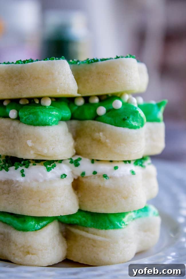 The Softest Sugar Cookies of Your Life from The Food Charlatan. A secret ingredient in this sugar cookies recipe makes these cookies the SOFTEST and most flavorful cookies of your life! And they even hold their shape after baking, so you get exactly what you want instead of sad blob cookies. #sugarcookies #cookies #frosting #soft #recipe #holiday #christmas #easter #halloween #fourthofjuly #stpatricksday #cookies #easy soft frosted sugar cookies stacked, frosted with green and white buttercream frosting and sprinkles.