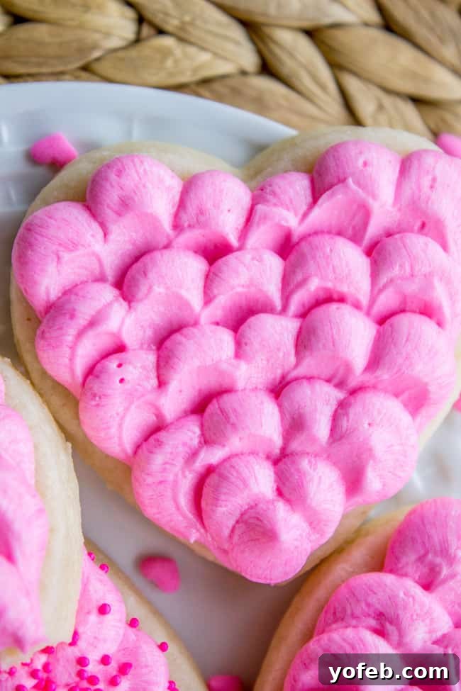 The Softest Sugar Cookies of Your Life from The Food Charlatan. A secret ingredient in this sugar cookies recipe makes these cookies the SOFTEST and most flavorful cookies of your life! And they even hold their shape after baking, so you get exactly what you want instead of sad blob cookies. #sugarcookies #cookies #frosting #soft #recipe #holiday #christmas #easter #halloween #fourthofjuly #stpatricksday #cookies #easy close up of sugar cookies with dollops of pink buttercream frosting.