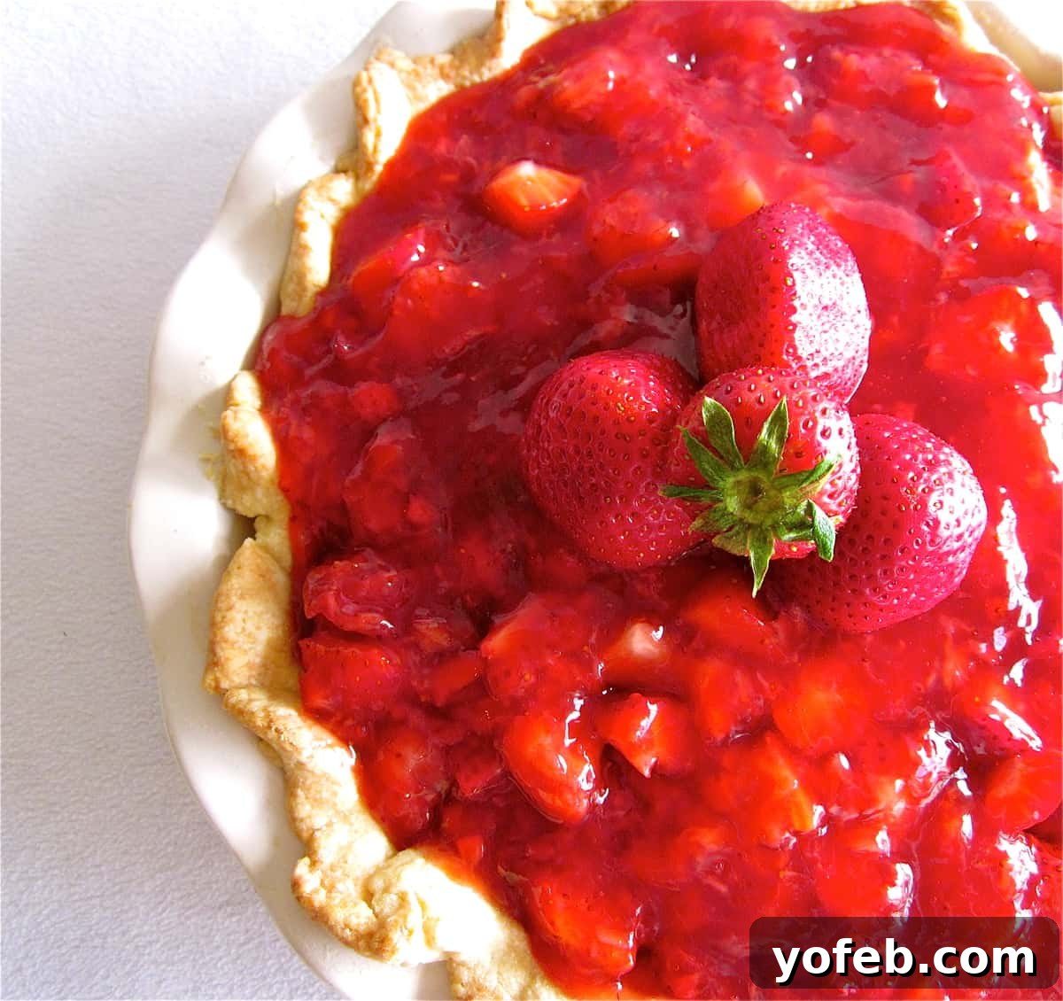 Strawberry Glace Pie Main Image A beautifully composed shot of a slice of Strawberry Glace Pie with a scoop of whipped cream on top, and the whole pie in the background.