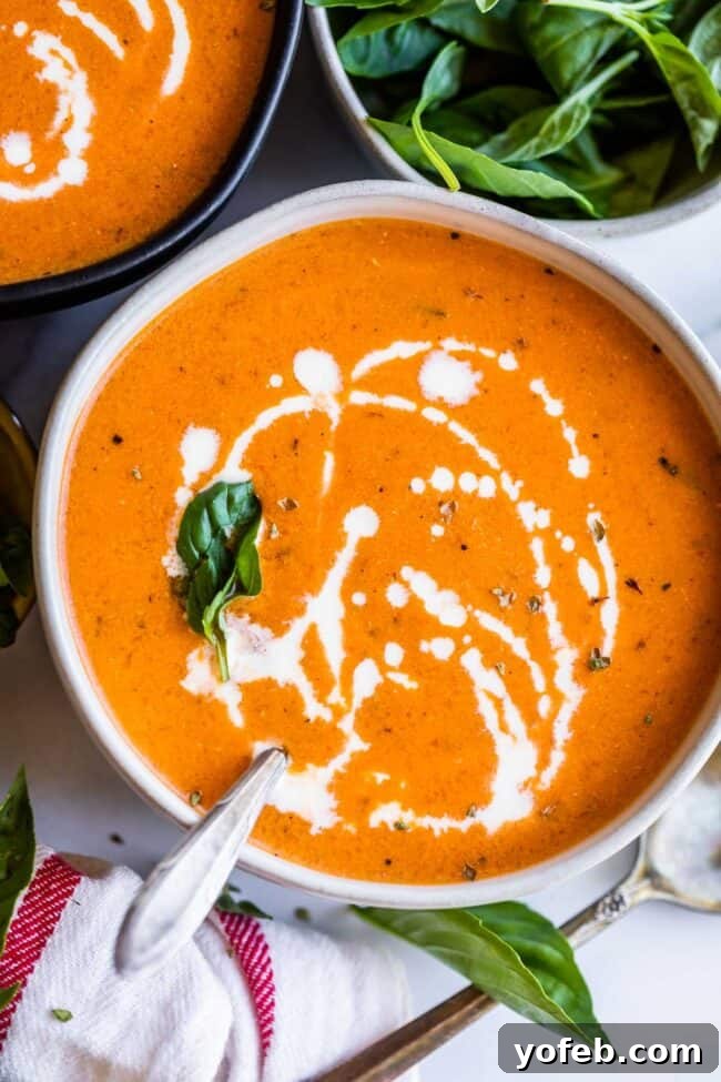 A bowl of creamy tomato soup garnished with fresh basil leaves, ready to be enjoyed.