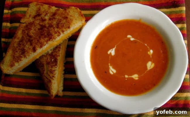 Homemade tomato soup in a bowl with heart shaped swirls of cream and a grilled cheese sandwich.