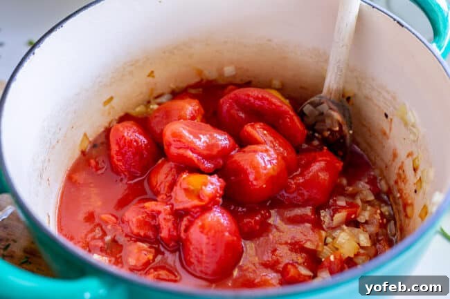 Whole canned tomatoes being added to a pot, a key step in making homemade tomato soup.