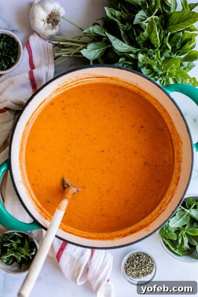 A large pot of creamy homemade tomato soup being stirred with a wooden spoon, showcasing its smooth texture.