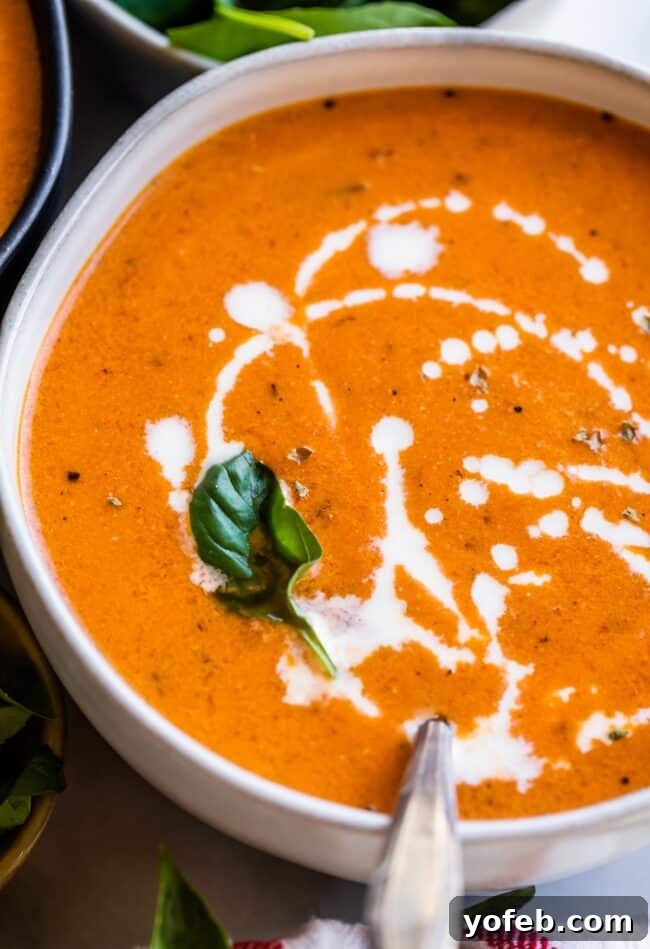 A mesmerizing swirl of heavy cream being drizzled into a bowl of creamy tomato soup, garnished with fresh basil.