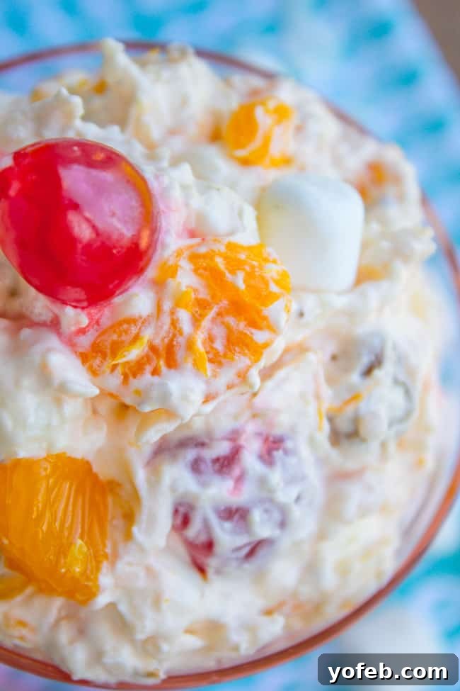 Heavenly Ambrosia Fruit Salad 6 A charming close-up of Ambrosia Salad in a pink glass dish, highlighting the colorful ingredients and creamy texture against a soft backdrop.